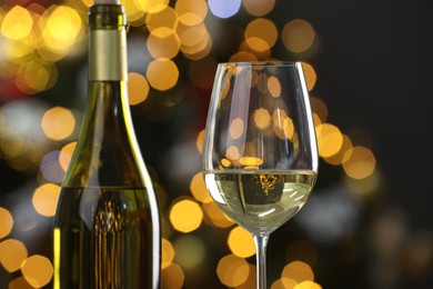 Photo of White wine in glass and bottle against blurred Christmas lights, closeup