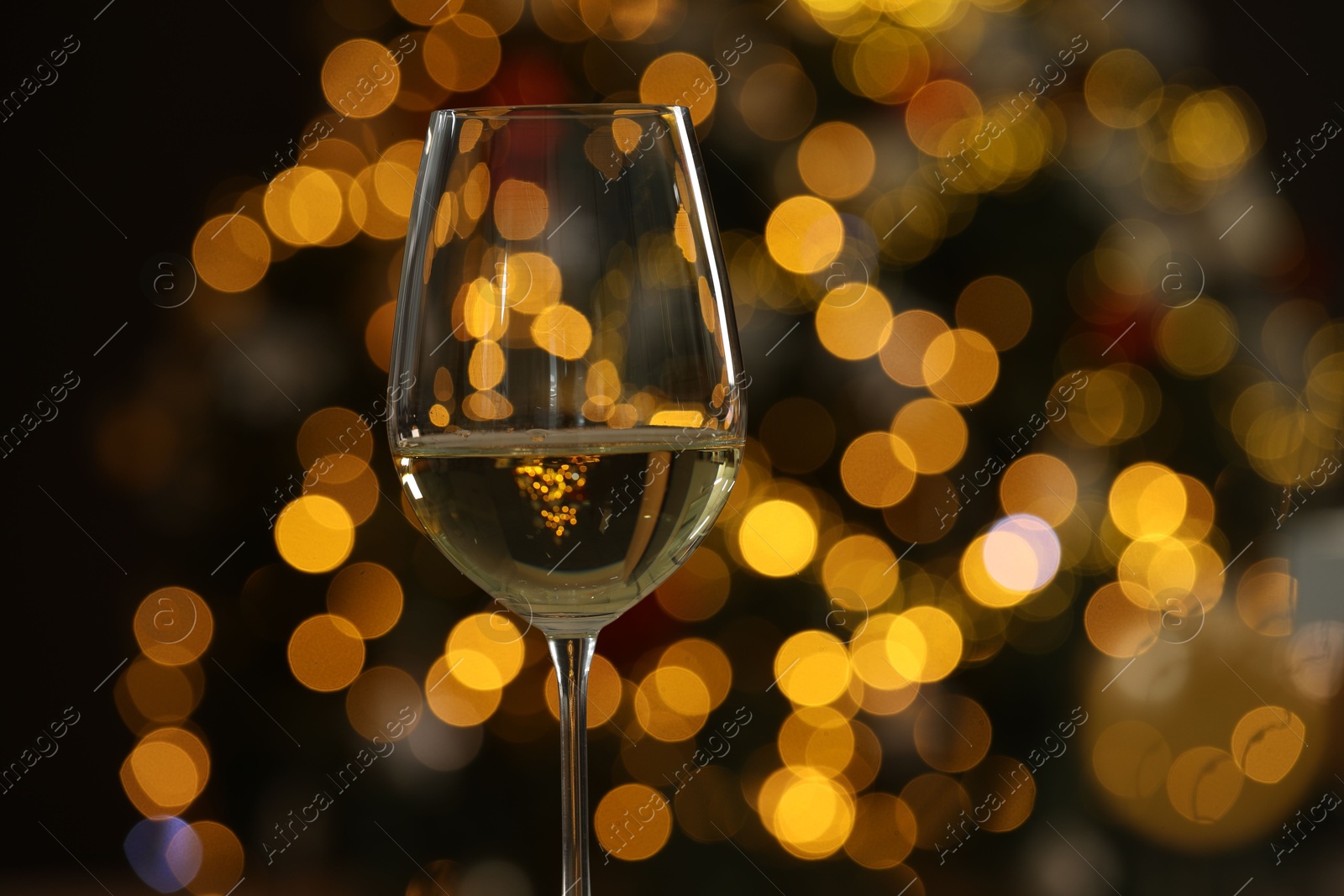 Photo of White wine in glass against blurred Christmas lights, closeup