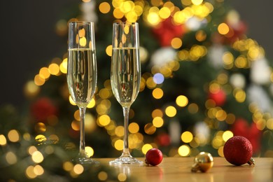 Photo of Champagne in glasses and festive ornaments on wooden table against blurred Christmas lights, space for text. Bokeh effect