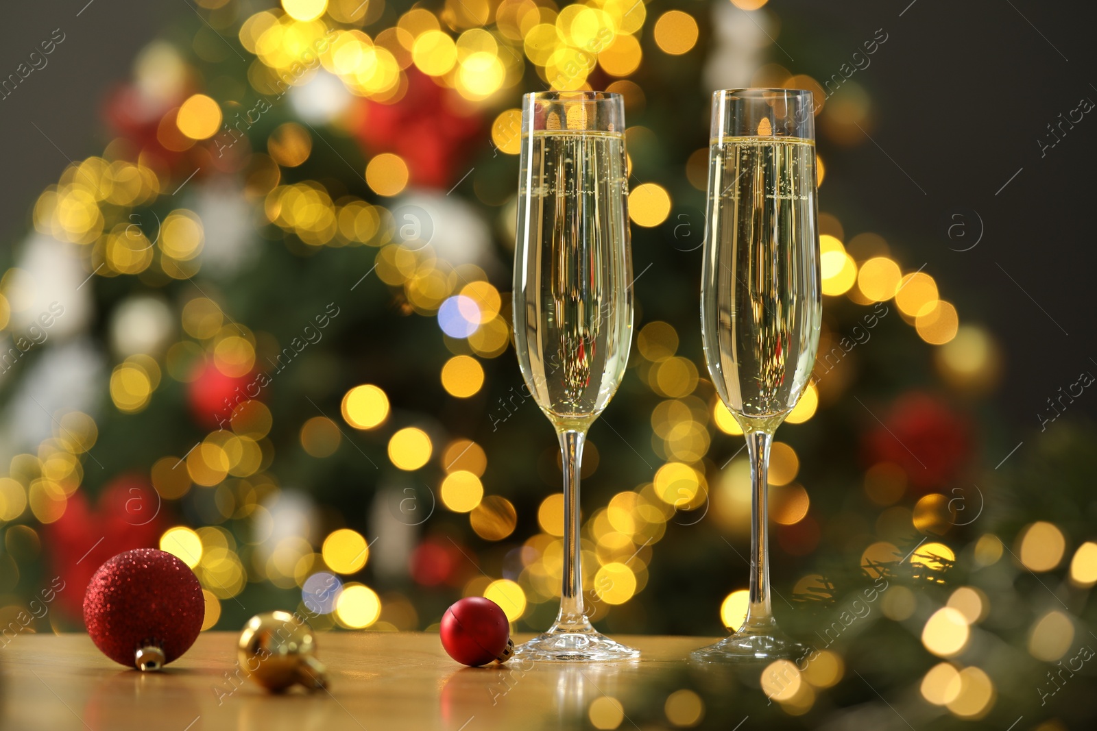 Photo of Champagne in glasses and festive ornaments on wooden table against blurred Christmas lights, space for text. Bokeh effect