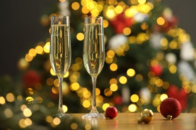 Photo of Champagne in glasses and festive ornaments on wooden table against blurred Christmas lights, space for text. Bokeh effect