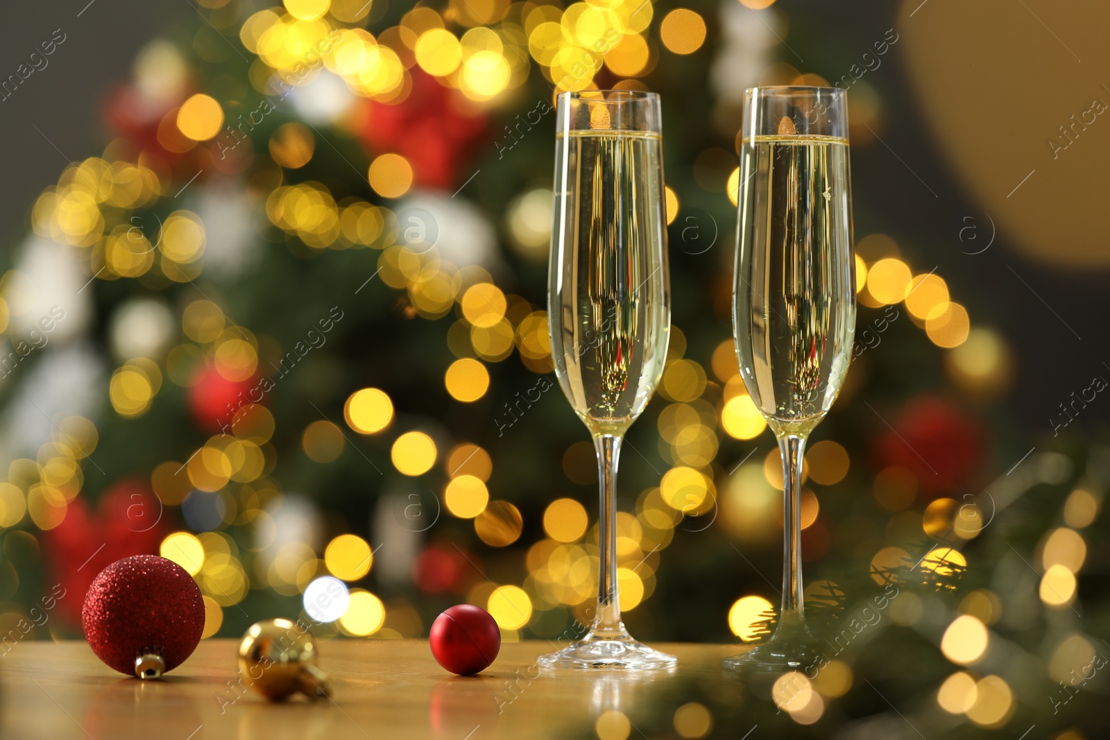 Photo of Champagne in glasses and festive ornaments on wooden table against blurred Christmas lights, space for text. Bokeh effect