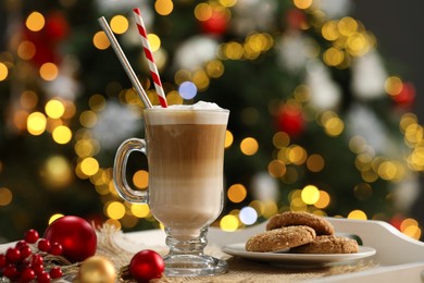 Photo of Aromatic coffee in glass, tasty cookies and decor on tray against blurred Christmas lights, bokeh effect