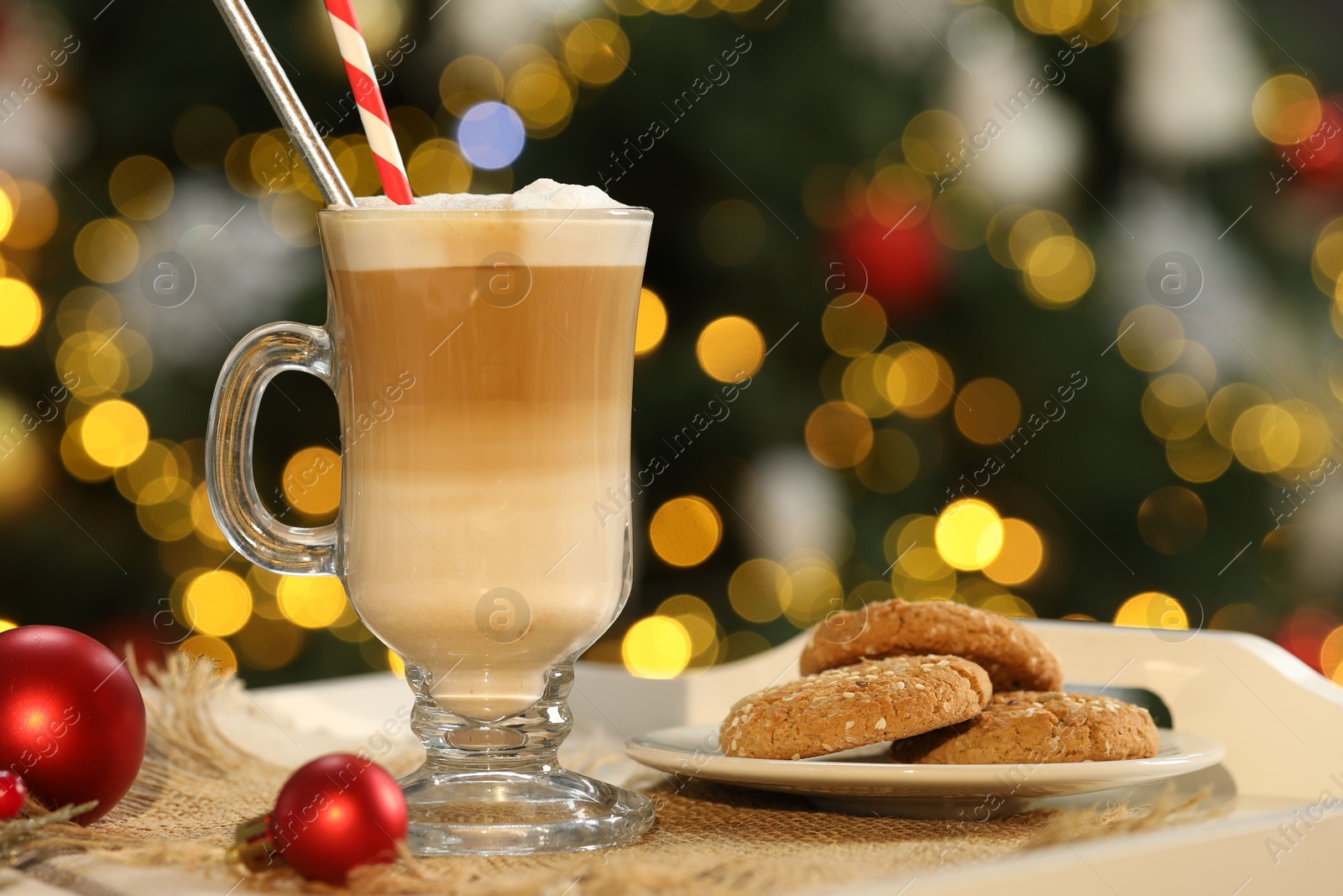 Photo of Aromatic coffee in glass, tasty cookies and decor on tray against blurred Christmas lights, bokeh effect