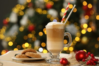 Photo of Aromatic coffee in glass, tasty cookies and decor on tray against blurred Christmas lights, bokeh effect