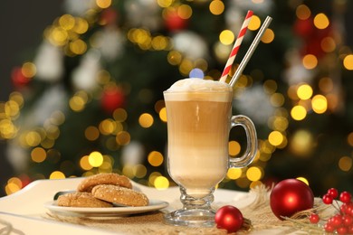 Photo of Aromatic coffee in glass, tasty cookies and decor on tray against blurred Christmas lights, bokeh effect