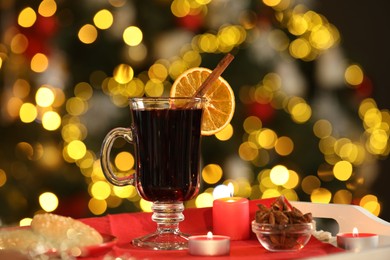 Photo of Aromatic mulled wine in glass cup, anise, cookies and burning candles on tray against blurred Christmas lights, bokeh effect