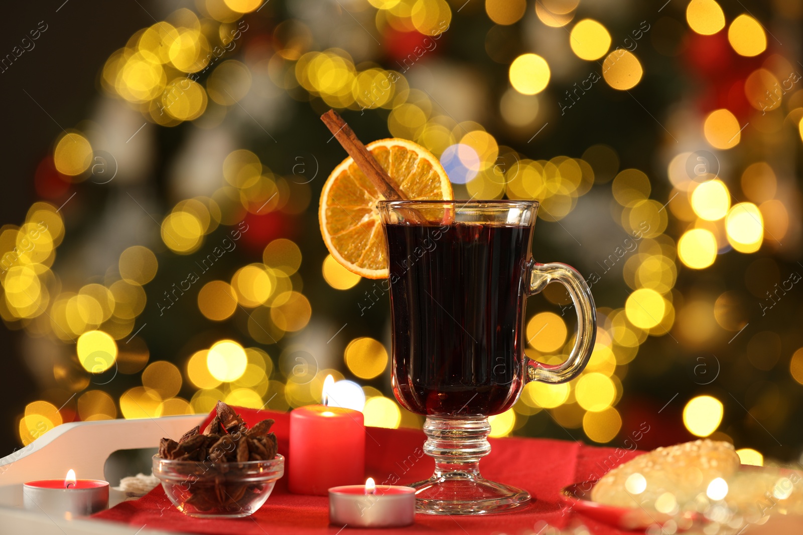 Photo of Aromatic mulled wine in glass cup, anise, cookies and burning candles on tray against blurred Christmas lights, bokeh effect