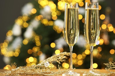 Photo of Champagne in glasses and decor on table against blurred Christmas lights, space for text. Bokeh effect