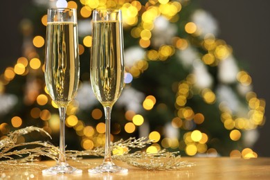 Photo of Champagne in glasses and decor on table against blurred Christmas lights, space for text. Bokeh effect