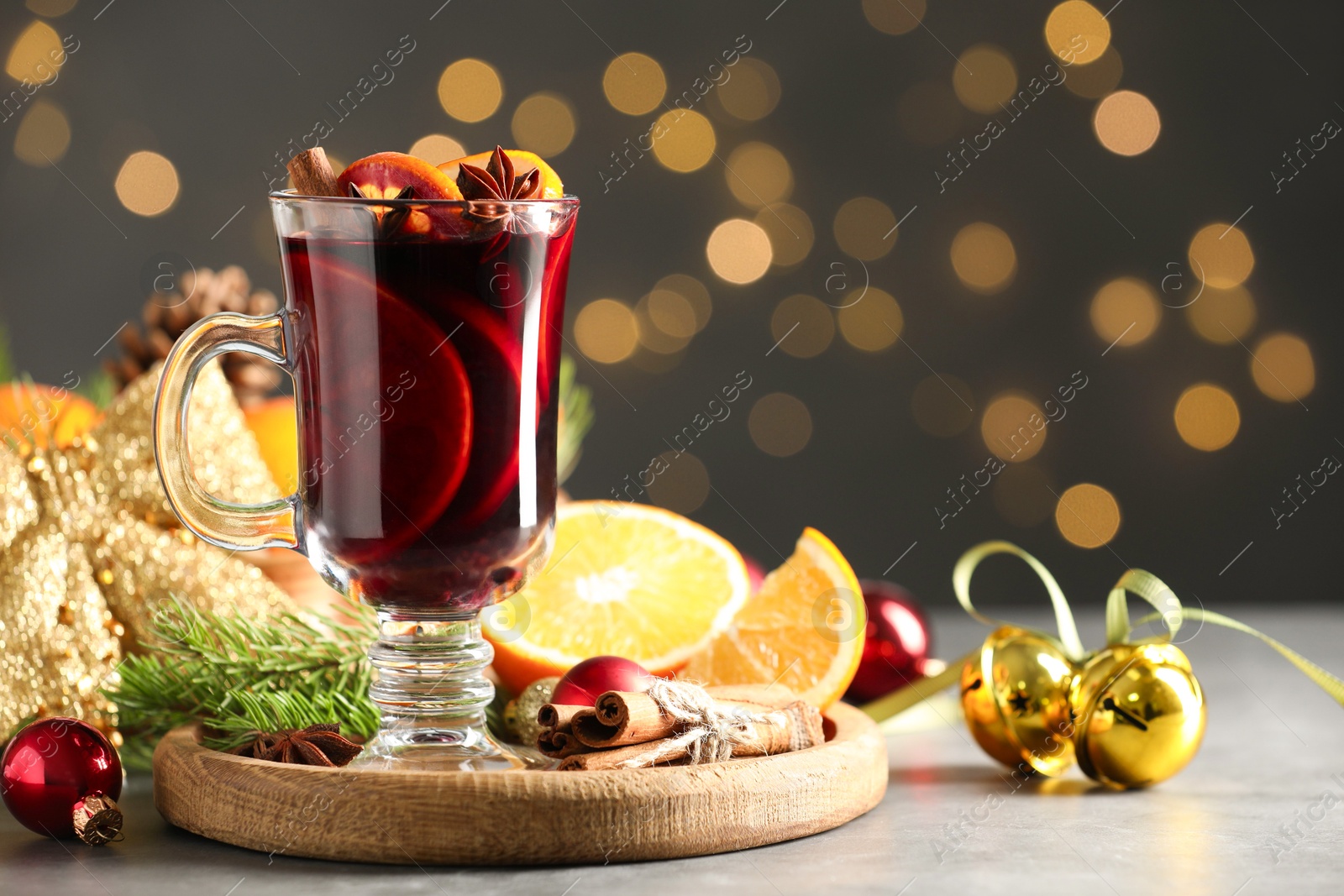 Photo of Tasty mulled wine, spices and Christmas decor on light table against blurred lights, closeup