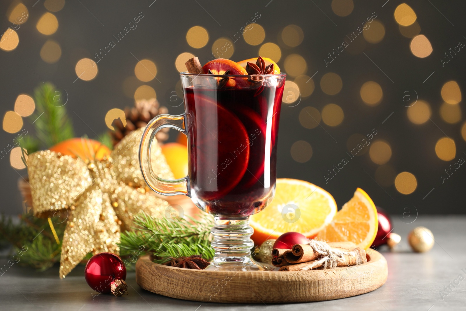 Photo of Tasty mulled wine, spices and Christmas decor on light table against blurred lights, closeup