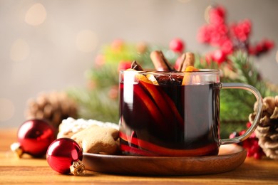 Photo of Cup of tasty mulled wine with spices and Christmas decor on wooden table, closeup