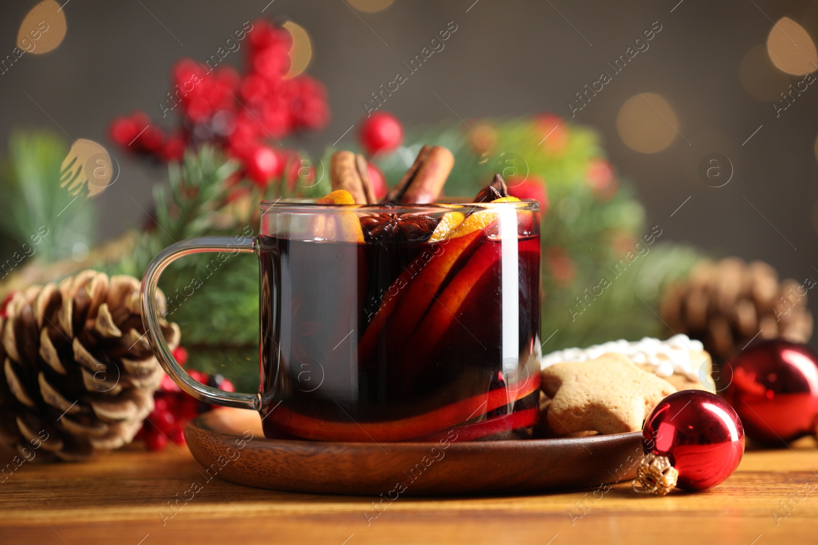 Photo of Cup of tasty mulled wine with spices and Christmas decor on wooden table against blurred lights, closeup