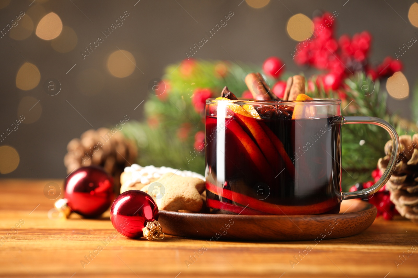 Photo of Cup of tasty mulled wine with spices and Christmas decor on wooden table against blurred lights, closeup