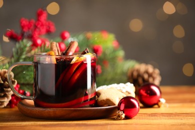 Photo of Cup of tasty mulled wine with spices and Christmas decor on wooden table against blurred lights, closeup