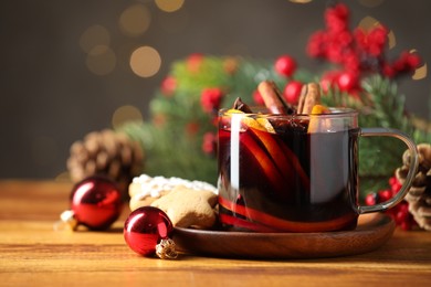 Photo of Cup of tasty mulled wine with spices and Christmas decor on wooden table against blurred lights, closeup