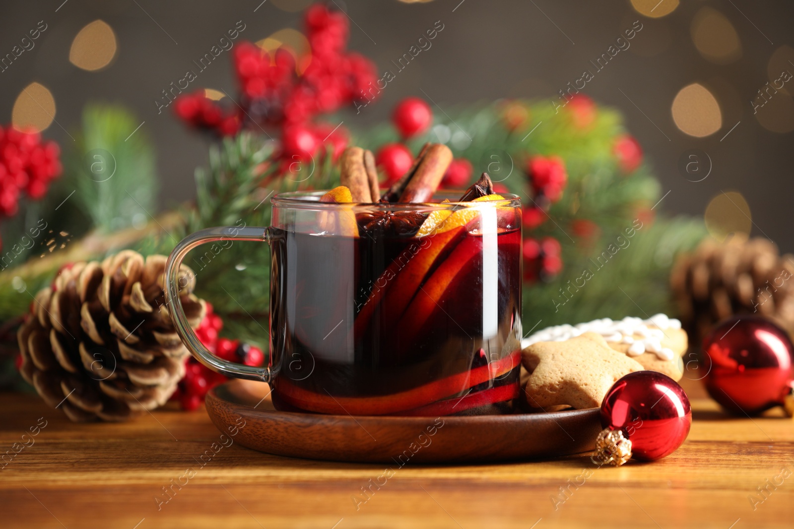 Photo of Cup of tasty mulled wine with spices and Christmas decor on wooden table against blurred lights, closeup