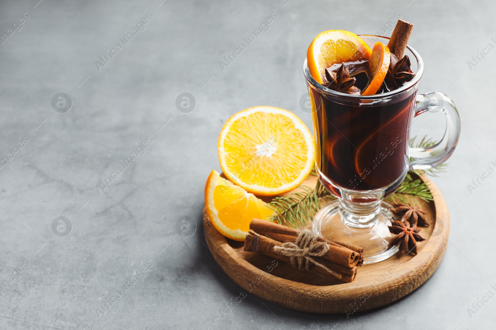 Photo of Tasty mulled wine with spices, fir branches and orange slices on grey table, closeup. Space for text