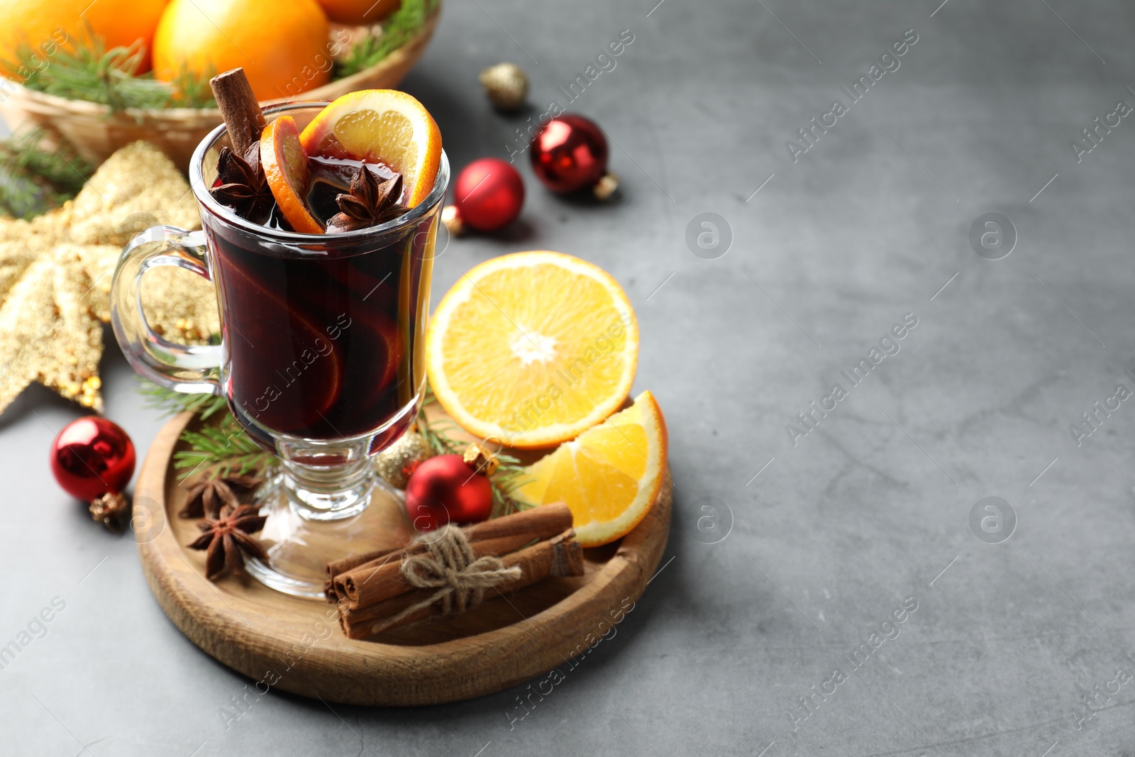 Photo of Tasty mulled wine with spices, orange slices and Christmas decor on grey table, closeup. Space for text