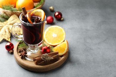 Photo of Tasty mulled wine with spices, orange slices and Christmas decor on grey table, closeup. Space for text