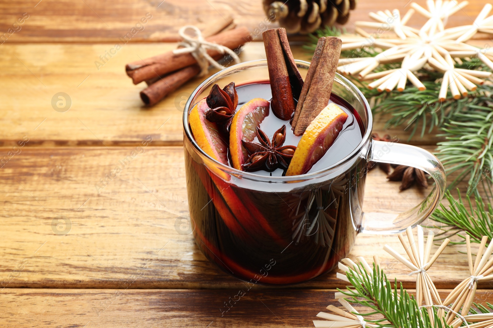 Photo of Tasty mulled wine with spices, orange slices and Christmas decor on wooden table, closeup