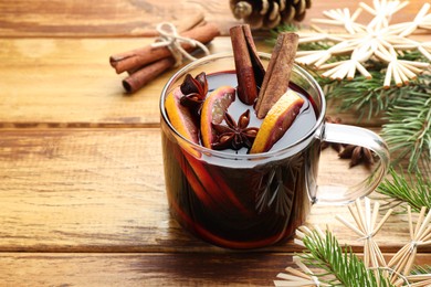 Photo of Tasty mulled wine with spices, orange slices and Christmas decor on wooden table, closeup