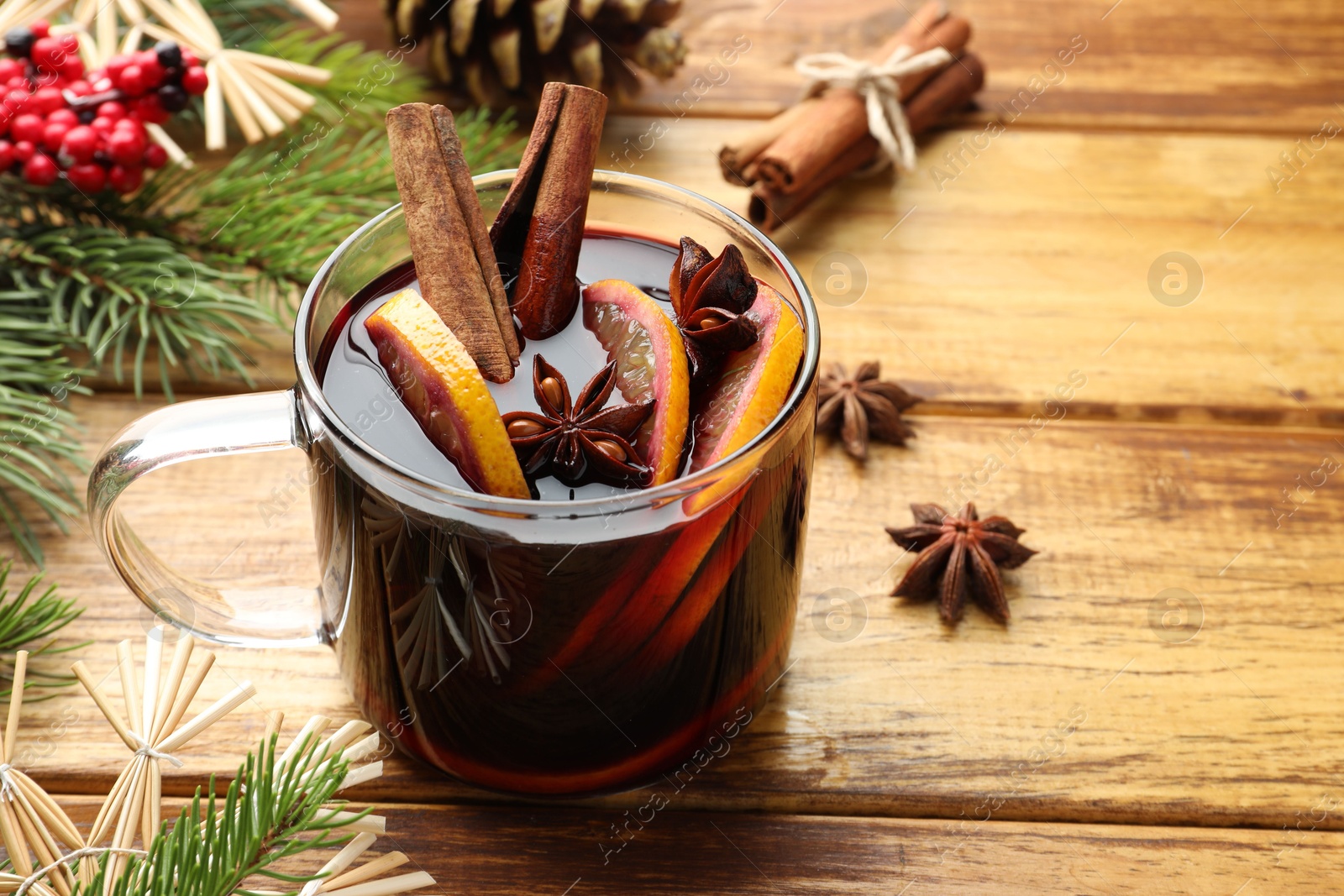 Photo of Tasty mulled wine with spices, orange slices and Christmas decor on wooden table, closeup