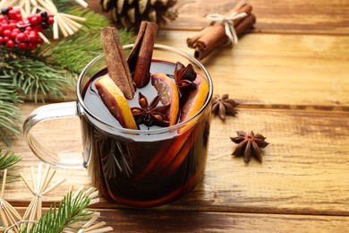 Photo of Tasty mulled wine with spices, orange slices and Christmas decor on wooden table, closeup