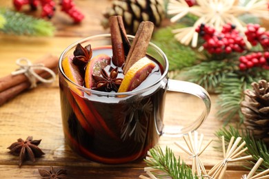 Photo of Tasty mulled wine with spices, orange slices and Christmas decor on wooden table, closeup