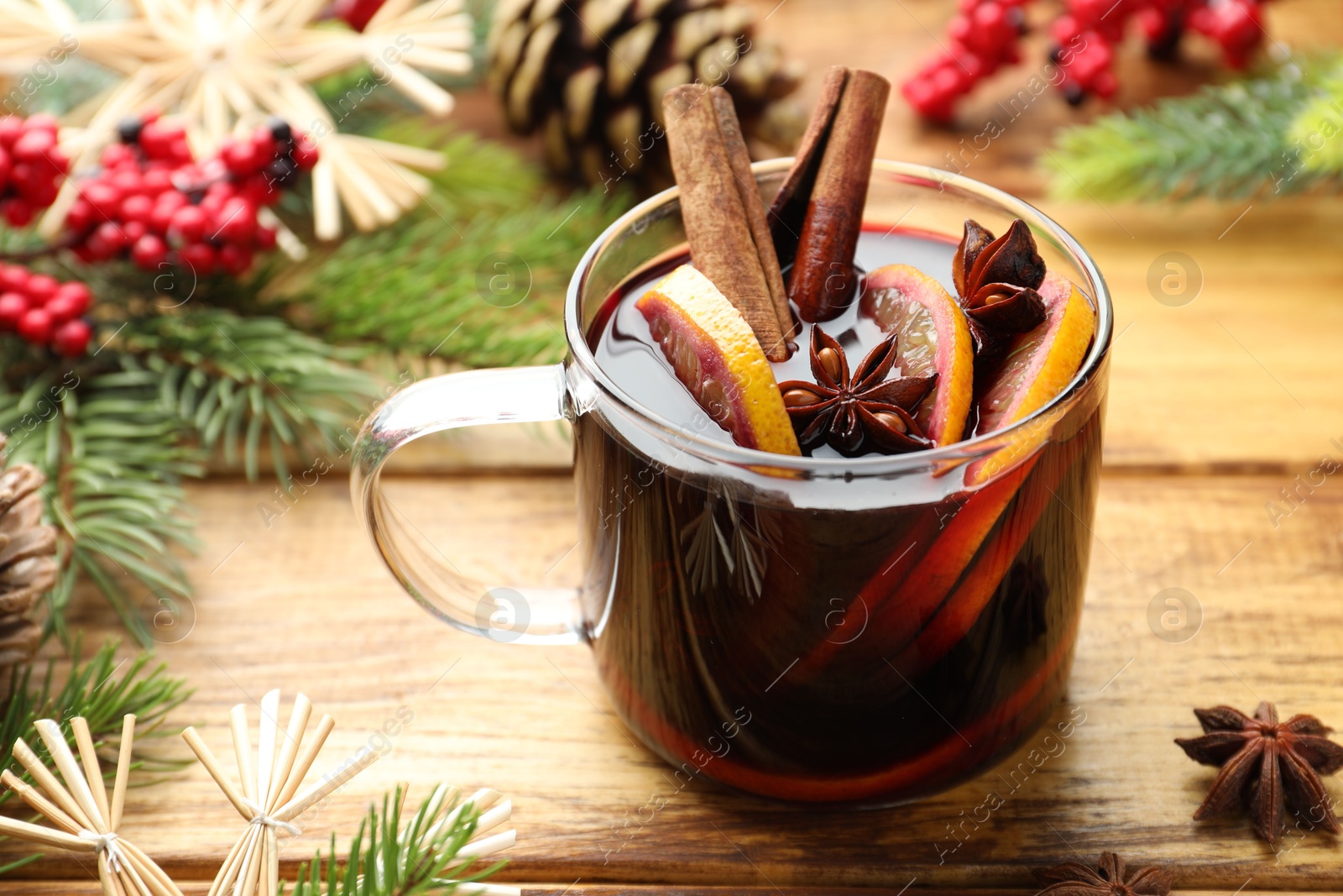 Photo of Tasty mulled wine with spices, orange slices and Christmas decor on wooden table, closeup