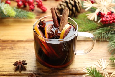 Photo of Tasty mulled wine with spices, orange slices and Christmas decor on wooden table, closeup