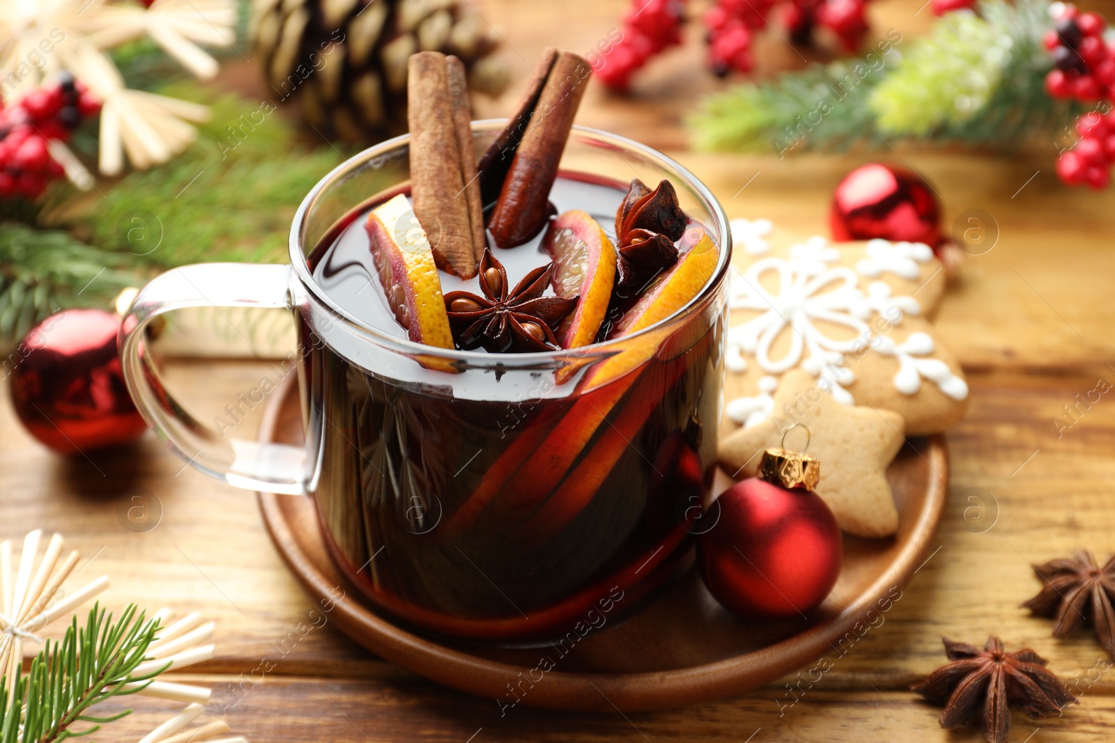 Photo of Tasty mulled wine with spices, orange slices and Christmas decor on wooden table, closeup