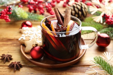 Photo of Tasty mulled wine with spices, orange slices and Christmas decor on wooden table, closeup