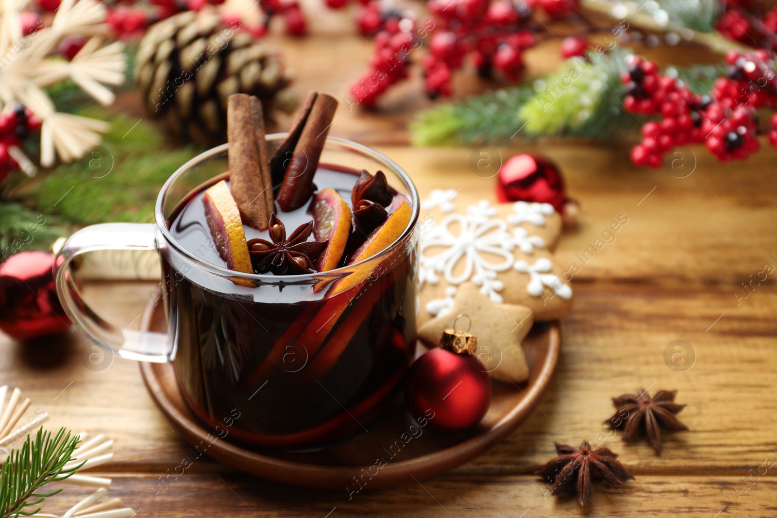 Photo of Tasty mulled wine with spices, orange slices and Christmas decor on wooden table, closeup