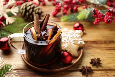 Photo of Tasty mulled wine with spices, orange slices and Christmas decor on wooden table, closeup