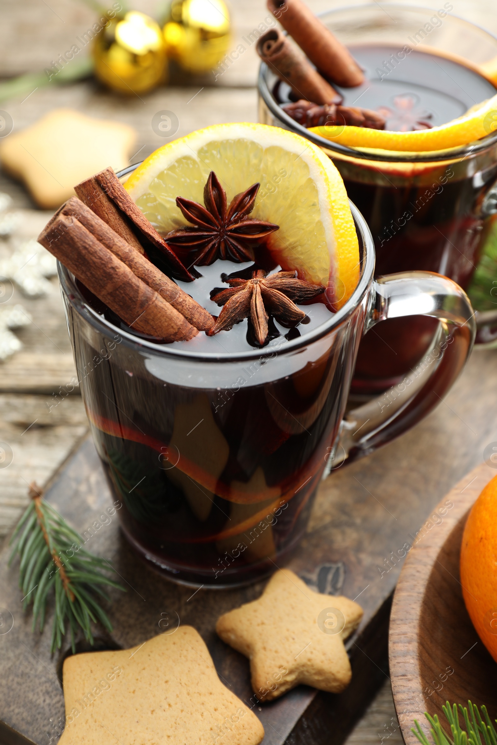 Photo of Tasty mulled wine with spices, orange slices, cookies and Christmas decor on wooden table, closeup