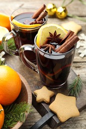 Photo of Tasty mulled wine with spices, orange slices, cookies and Christmas decor on wooden table, closeup