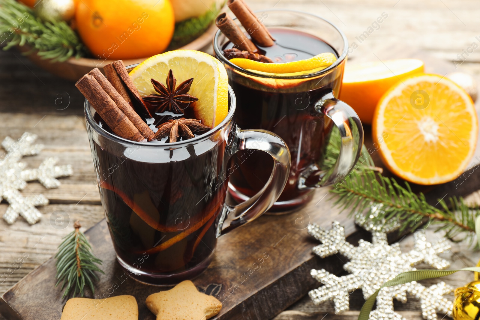 Photo of Tasty mulled wine with spices, orange slices, cookies and Christmas decor on wooden table, closeup