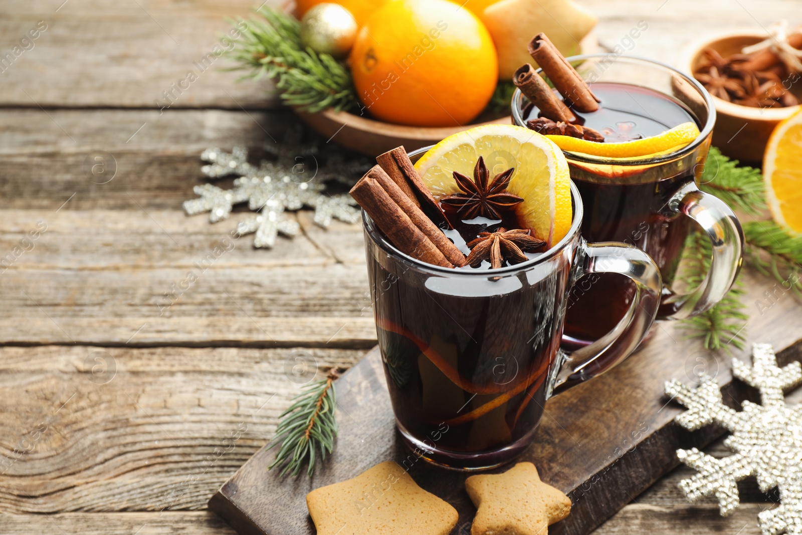 Photo of Tasty mulled wine with spices, orange slices, cookies and Christmas decor on wooden table, closeup. Space for text