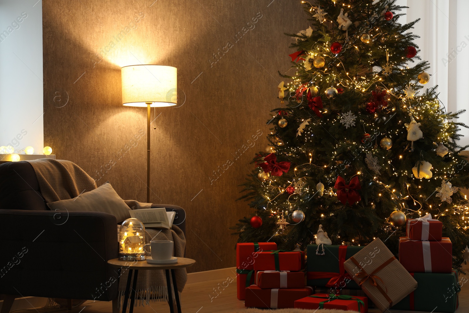 Photo of Christmas tree with festive decor, presents, coffee table and armchair in cozy room