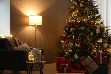 Photo of Christmas tree with festive decor, presents, coffee table and armchair in cozy room