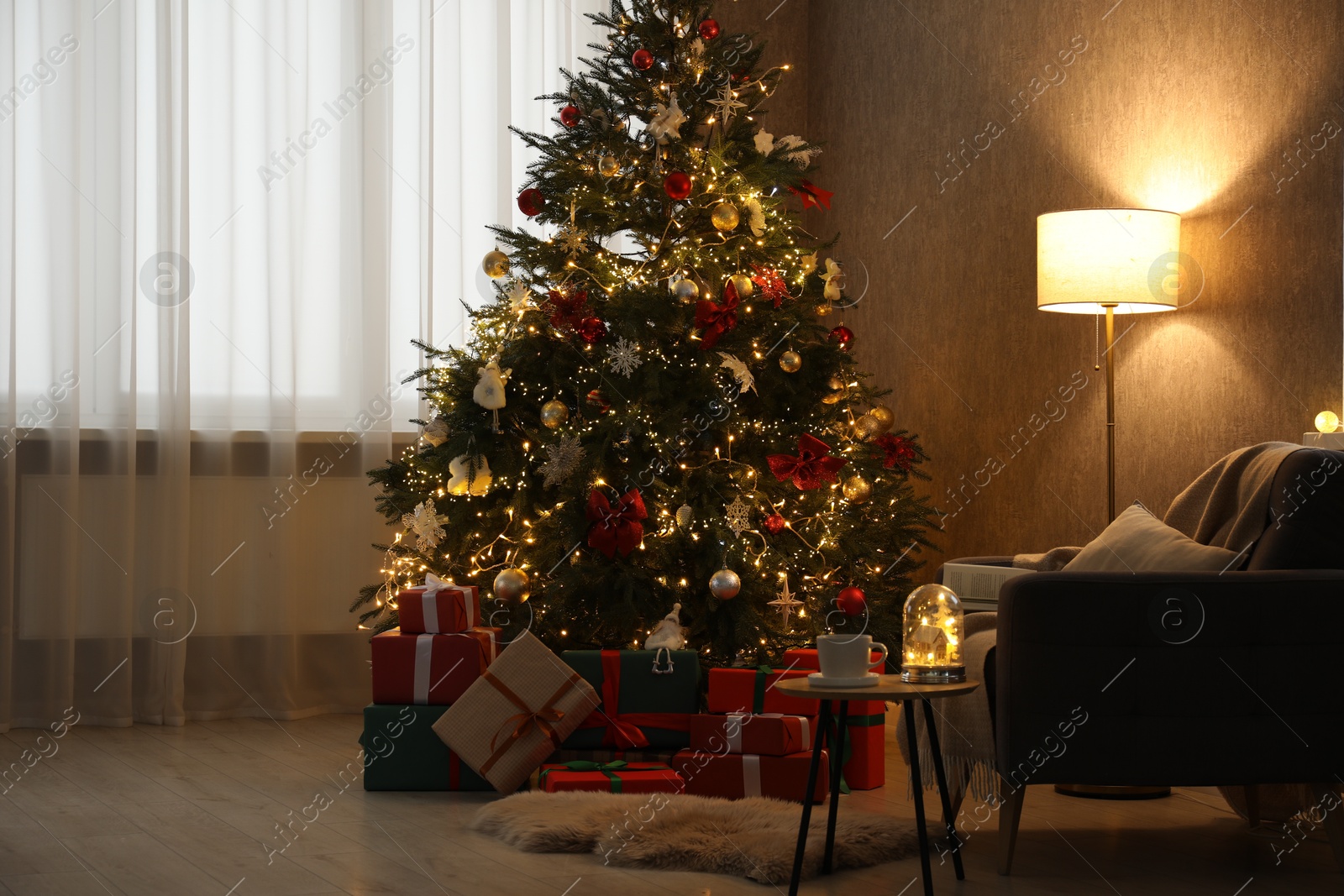 Photo of Christmas tree with festive decor, presents, coffee table and armchair in cozy room