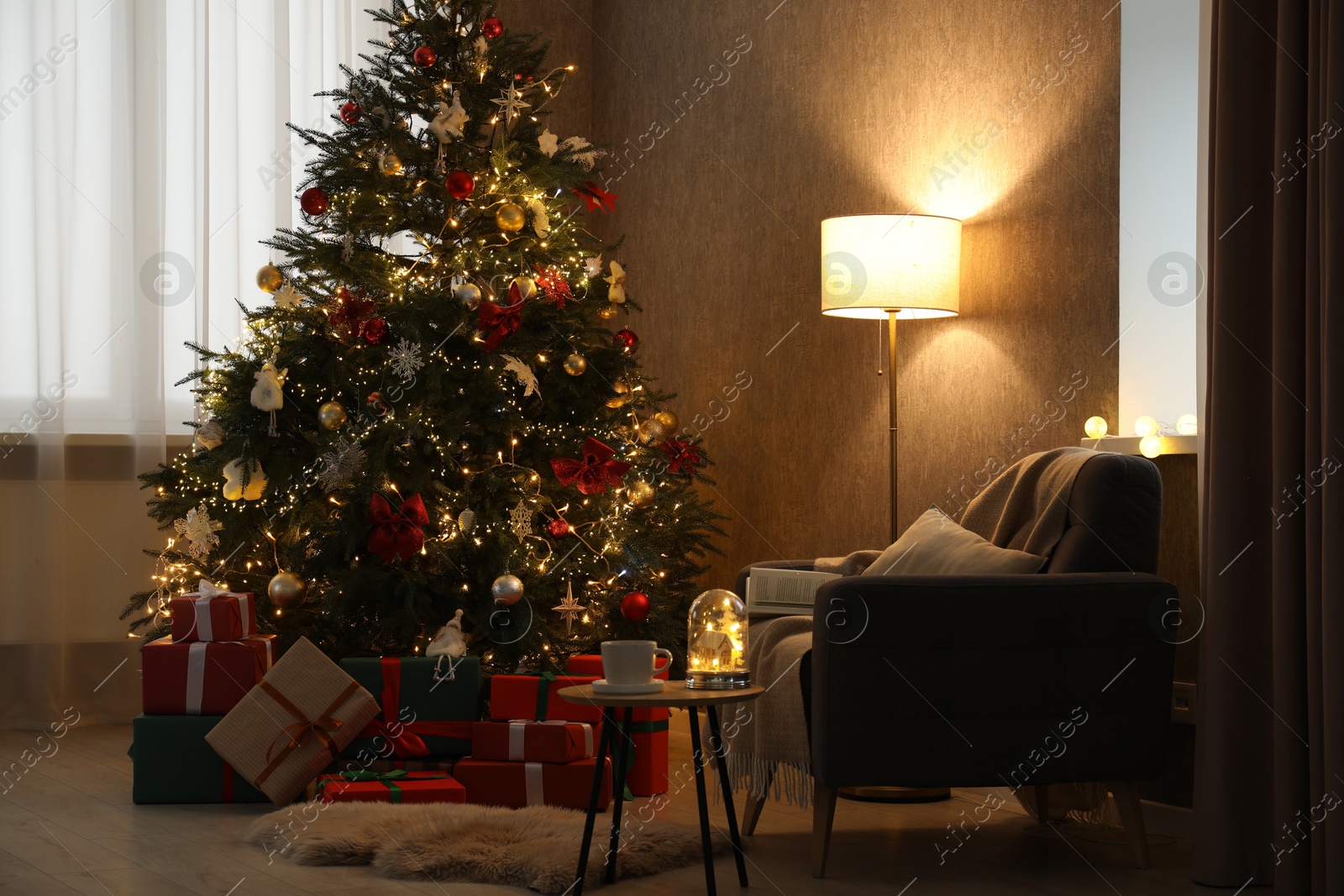 Photo of Christmas tree with festive decor, presents, coffee table and armchair in cozy room