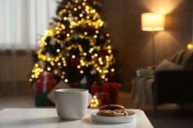 Photo of Cup of hot drink and cookies on white table in cozy room decorated for Christmas, closeup. Space for text