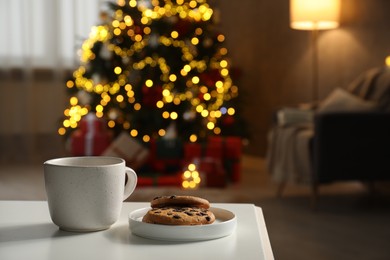 Photo of Cup of hot drink and cookies on white table in cozy room decorated for Christmas, closeup. Space for text