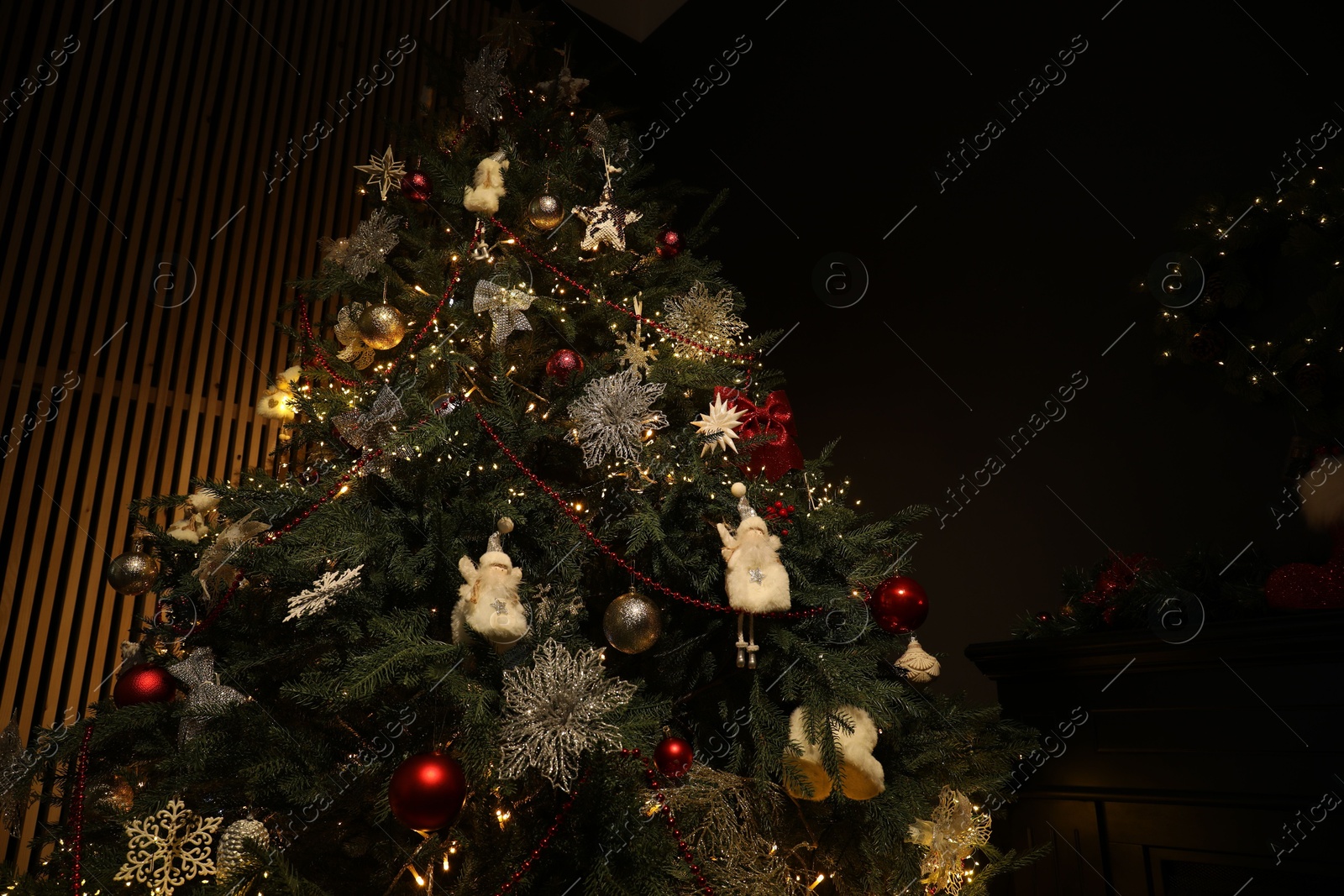 Photo of Christmas tree with festive decor in dark room, low angle view