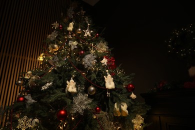 Photo of Christmas tree with festive decor in dark room, low angle view