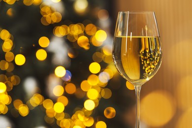 Photo of White wine in glass against blurred Christmas lights, space for text. Bokeh effect