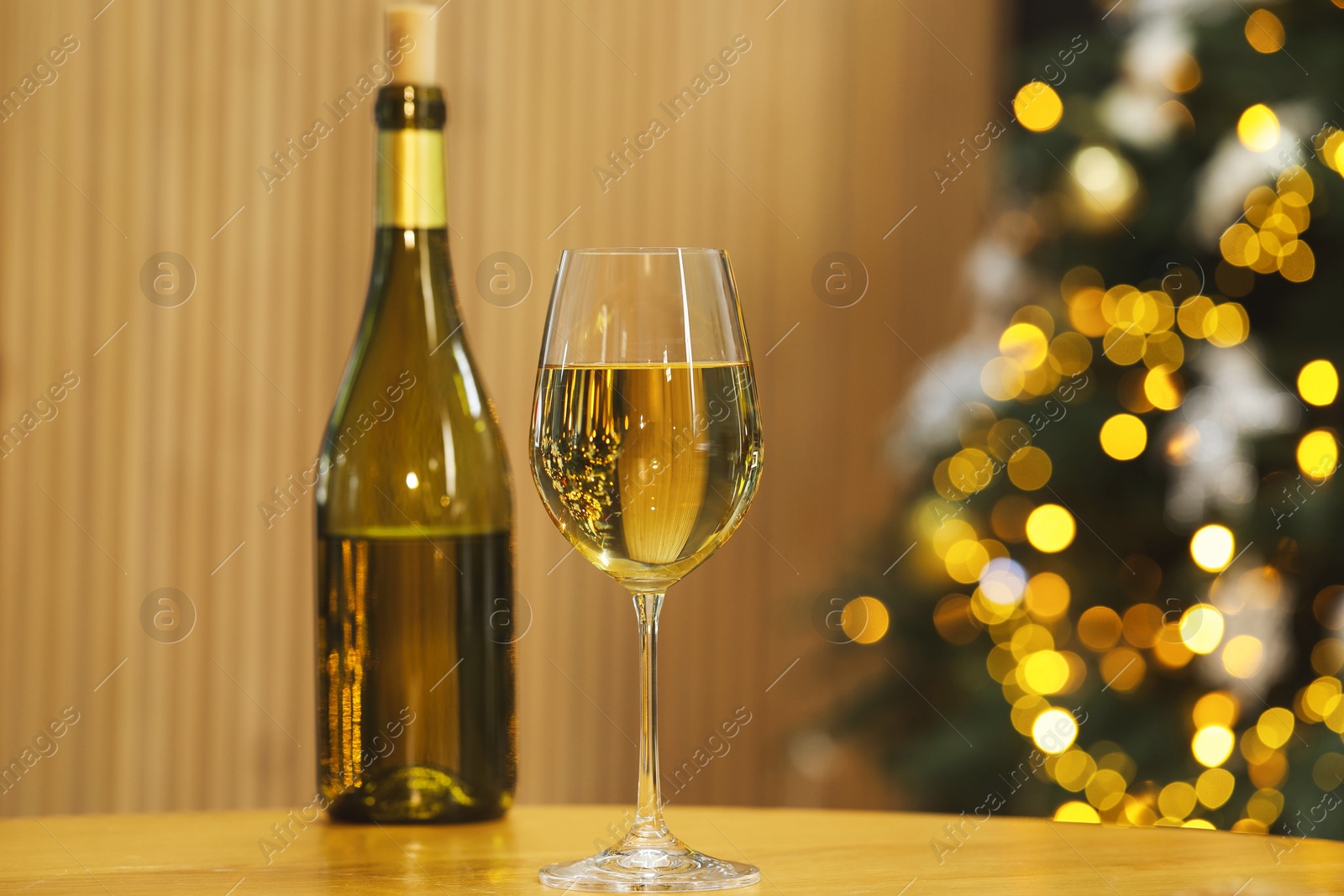 Photo of White wine in glass and bottle on table against blurred Christmas lights, space for text. Bokeh effect